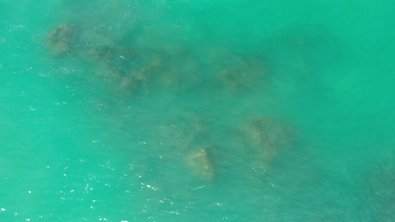 Overhead view in Los Cabos, Mexico of turquoise shallow water with brown coral or rock forms under the surface and no visible people.