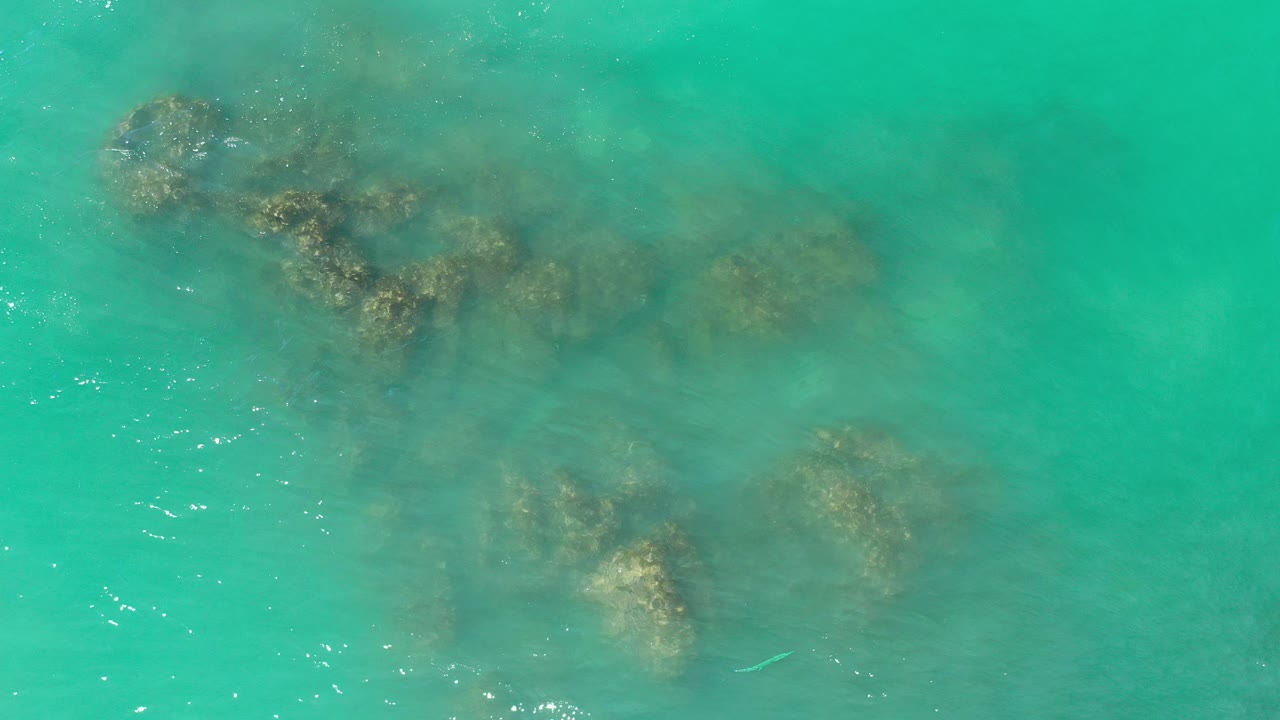 Overhead view of clear turquoise water and submerged rocks in Los Cabos, Mexico, with small surface ripples and no visible people.