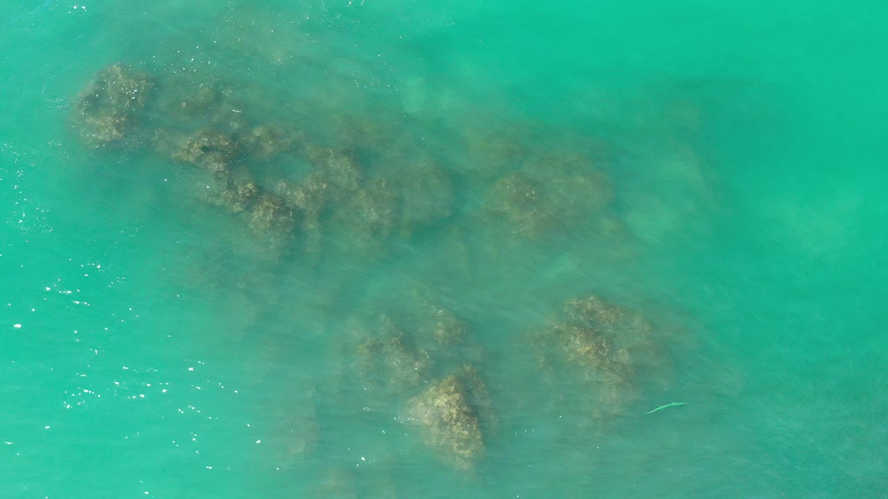 Overhead view of turquoise green water in Los Cabos, Mexico, with dark submerged reef patches near the upper left and no visible people.