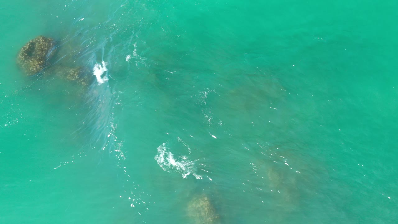 Turquoise water with reef rocks near the top edge and white wave foam at center.