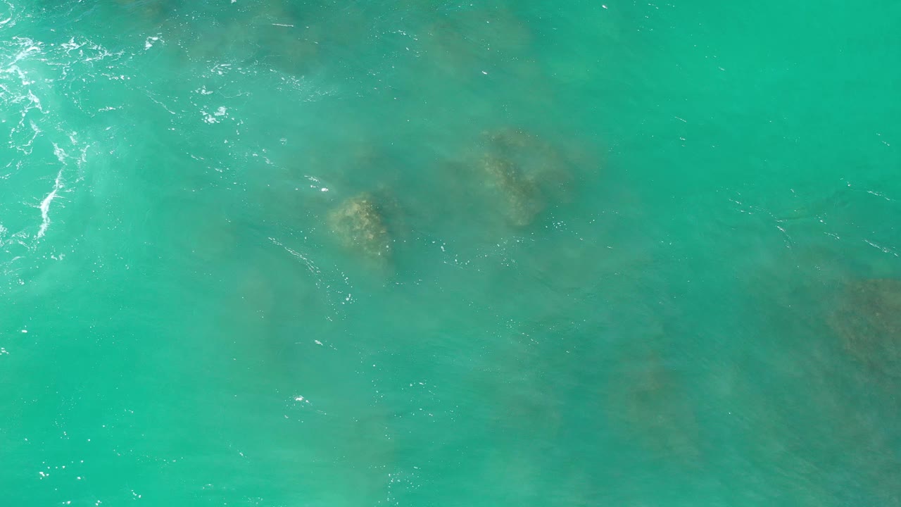 Sunlit turquoise water with a small rock form near the upper right.