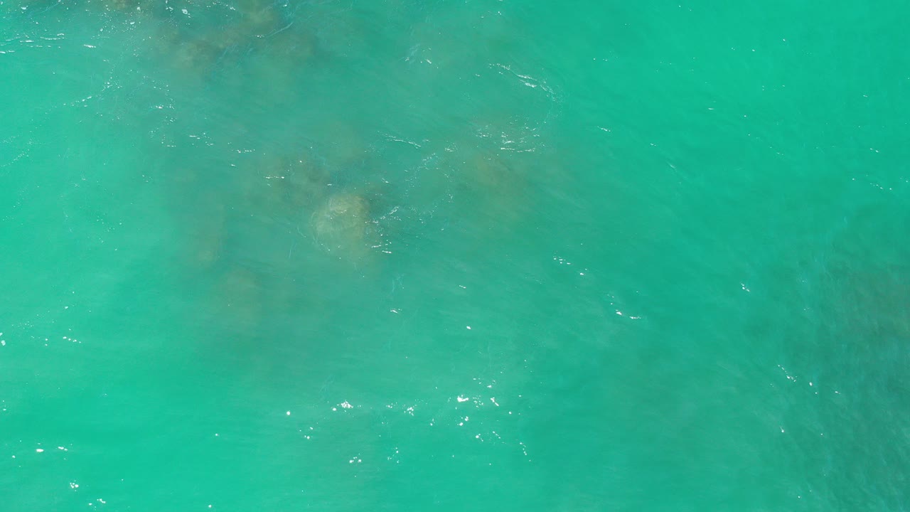 Overhead view of turquoise seawater in Los Cabos, Mexico, with faint submerged rocks visible beneath the surface and no visible people.