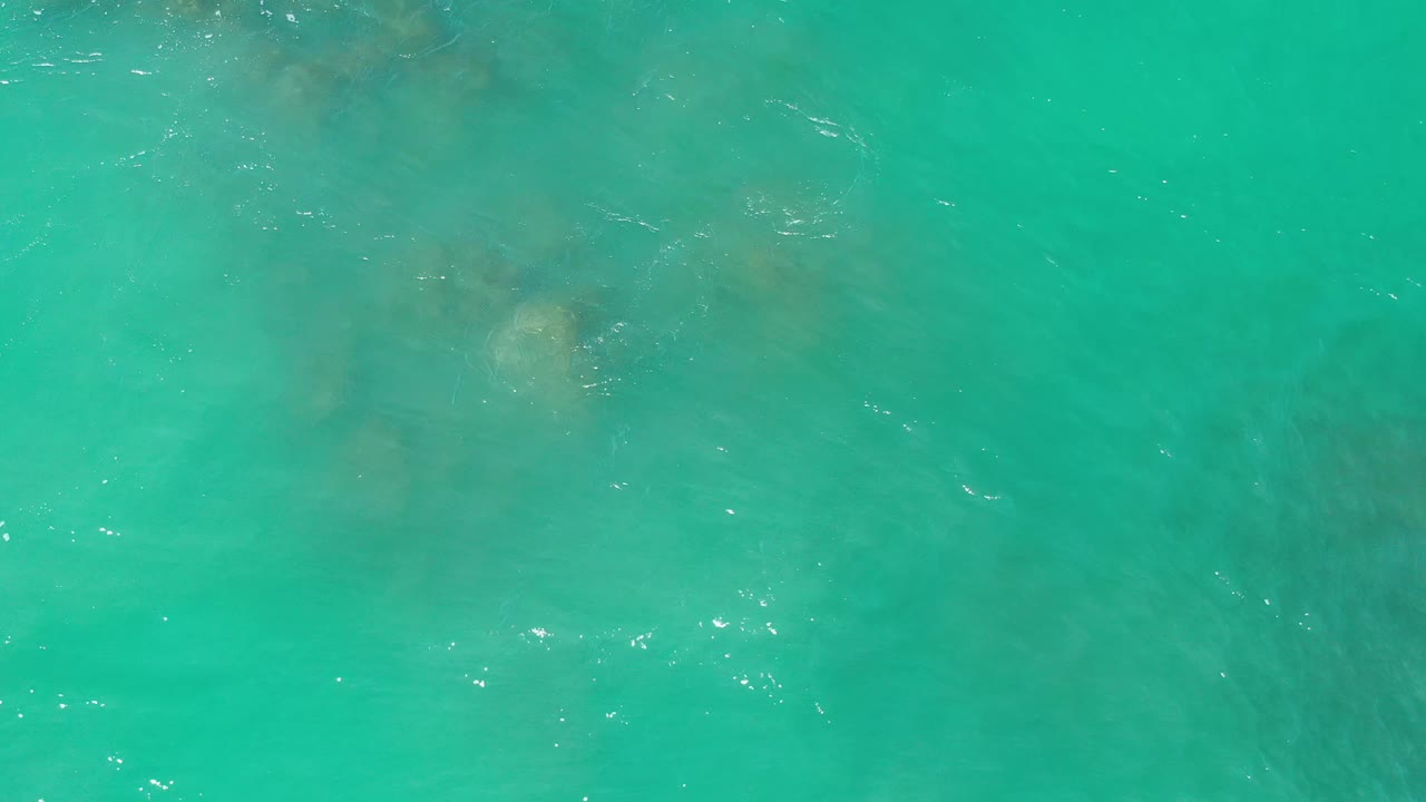 Turquoise sea fills the Los Cabos frame, with a pale underwater rock shape near the center-left and no visible people.