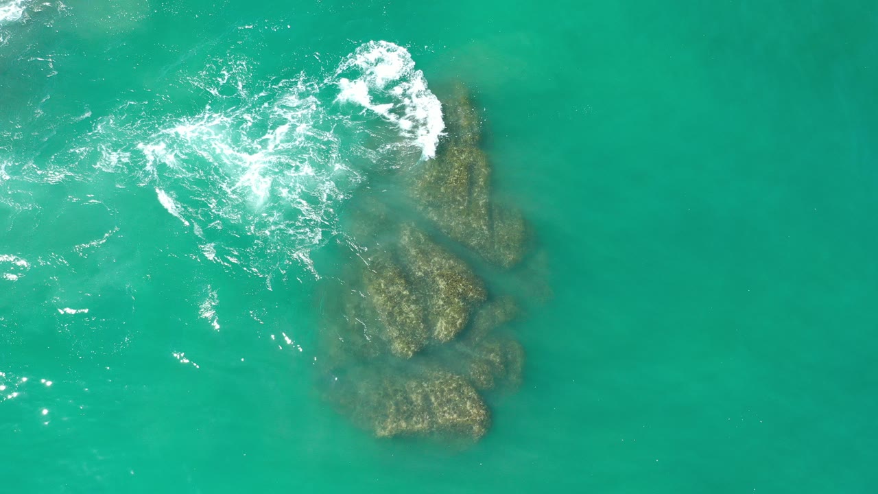 Overhead turquoise water with surf breaking over dark rocks.