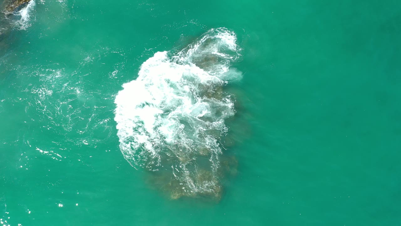 Wave foam covering the top of a brown rock in turquoise-green ocean.