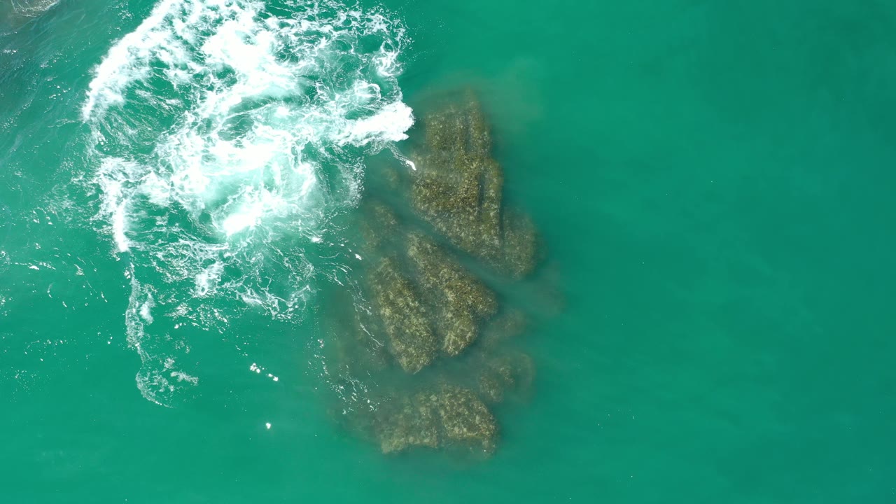 Whitewater breaking above a cluster of beach rocks