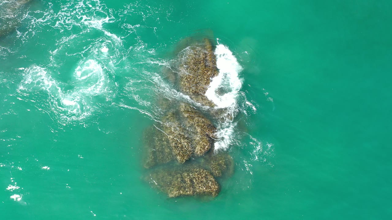 Overhead turquoise water with foam breaking around submerged rocks.