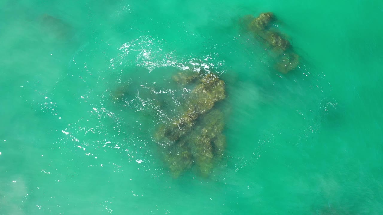 Clear ocean water with two submerged rock shapes and scattered white highlights.