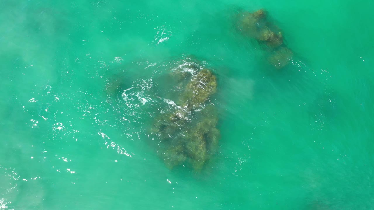 Aerial view of clear blue-green water with reef rocks and wave foam.