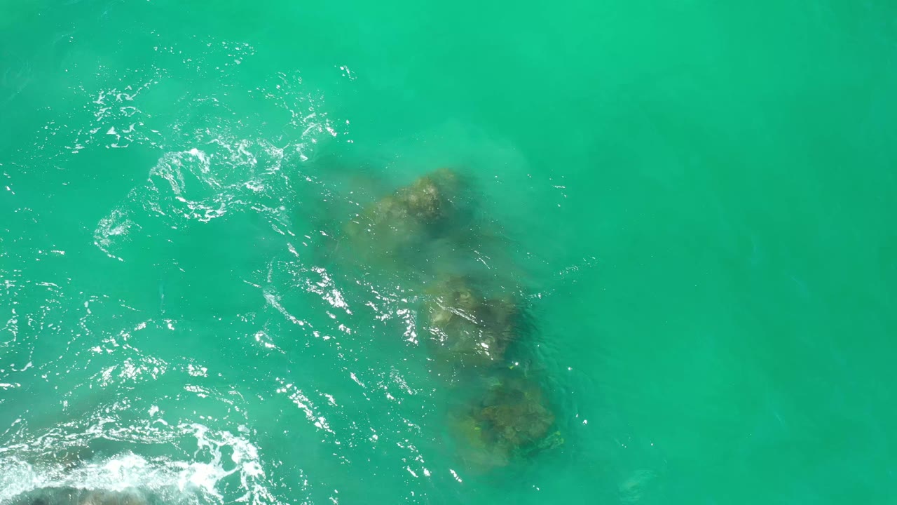 Second frame in Los Cabos, Mexico shows the same submerged rock formation shifted slightly in the composition, with bright white ripples spreading across the left side and no visible people.