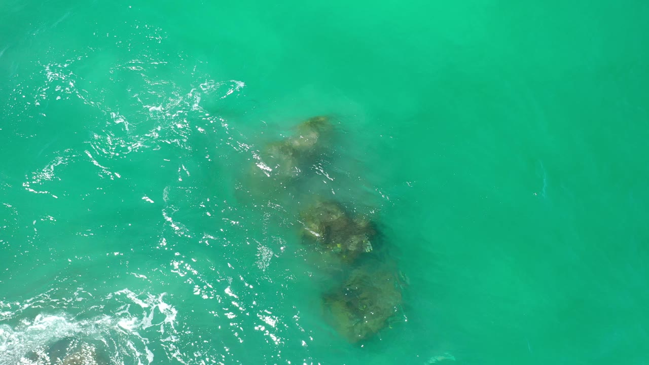 Turquoise ocean seen from above with rocks under the surface.
