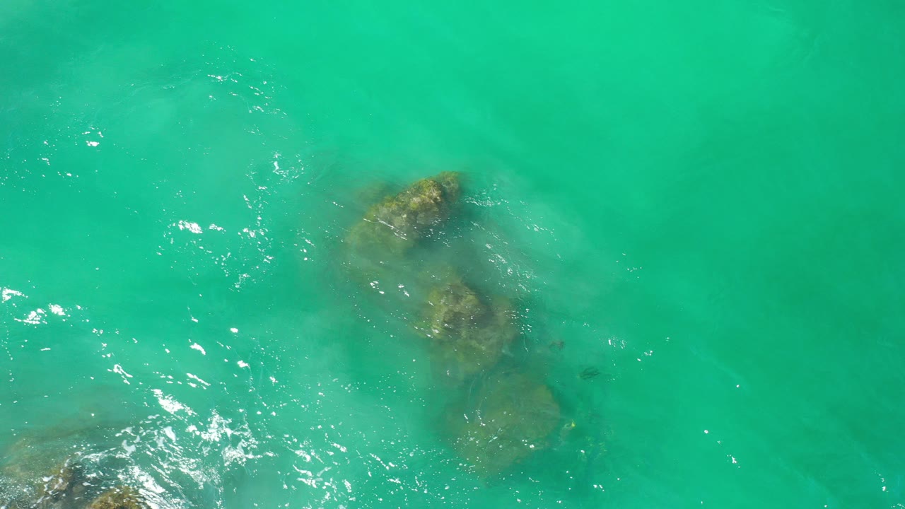 Turquoise water over submerged rocks with sun glints.