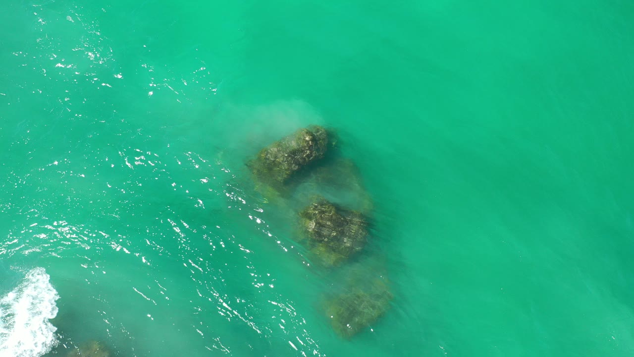 Overhead turquoise water with submerged rocks and foam at the lower left edge.