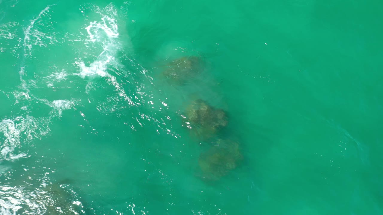Clear green water with white foam and rocks visible at right