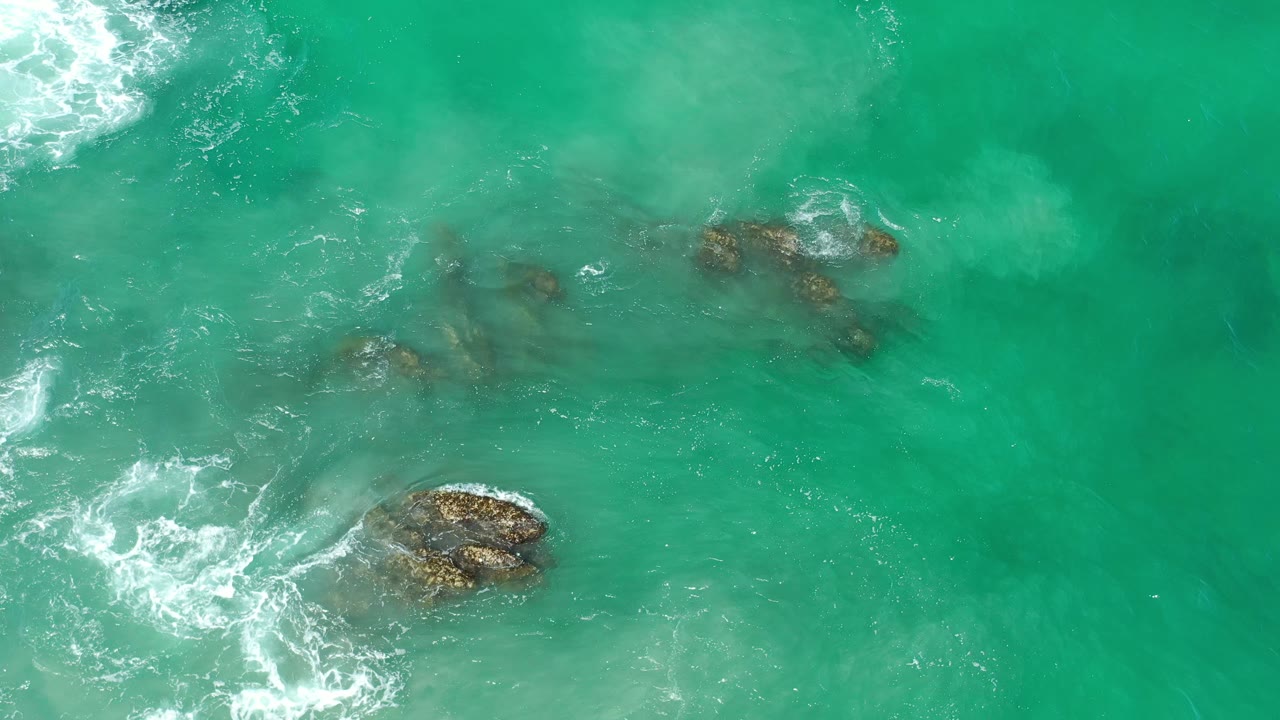 Green surf breaking softly around several rocks.