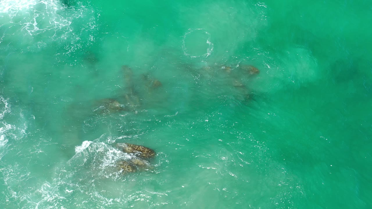 Aerial view of pale surf lines around rocks in green water