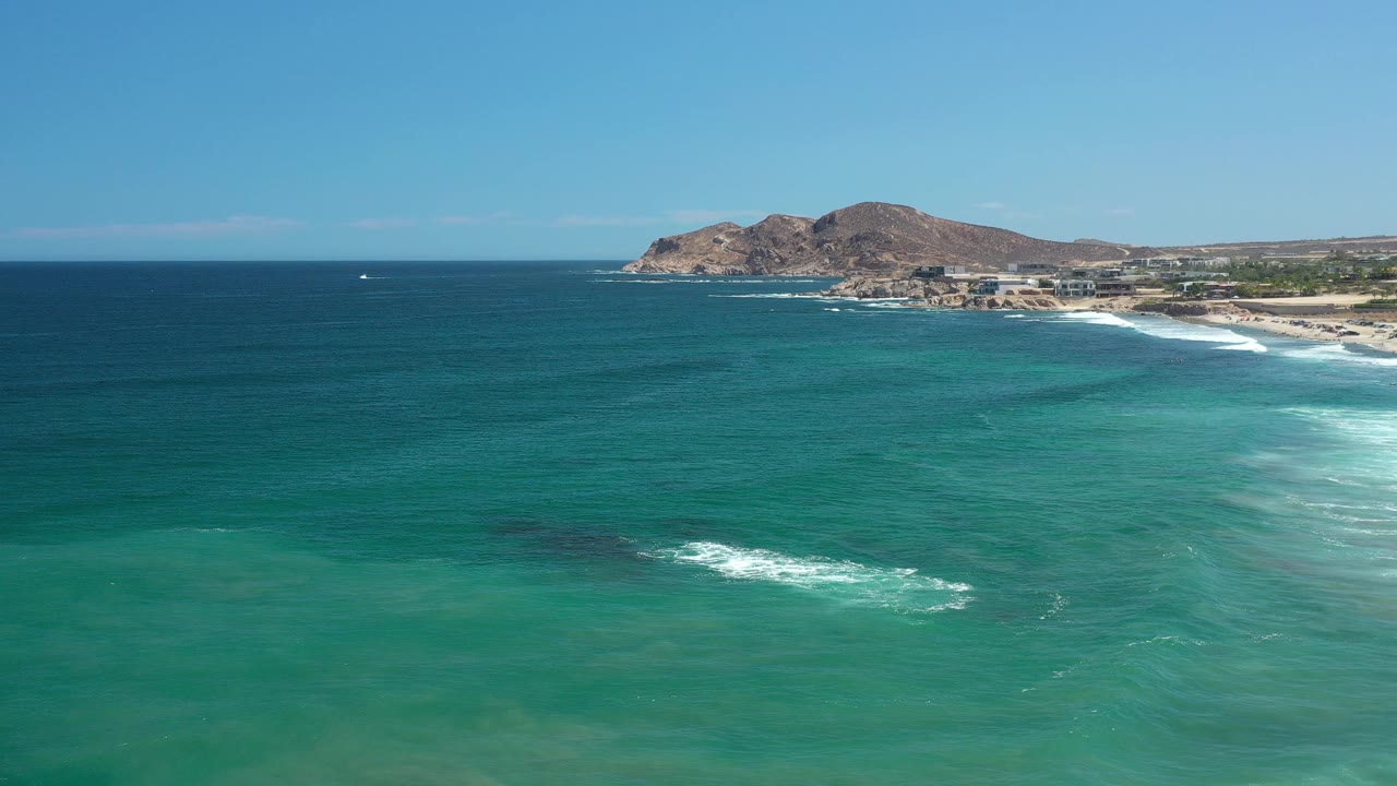 Opening frame of Los Cabos, Mexico with turquoise sea in the foreground, white surf near shore, rocky hills beyond the beach, and no visible people.