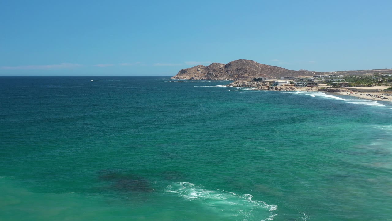 Ocean foreground with surf patches, distant beach buildings, and rocky headland.