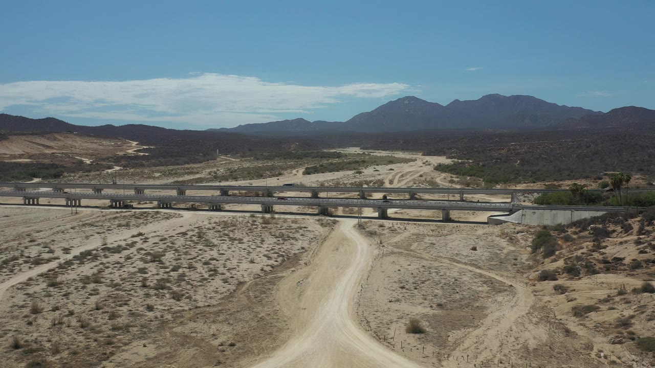Sunlit desert highway bridge with small cars and mountain backdrop.