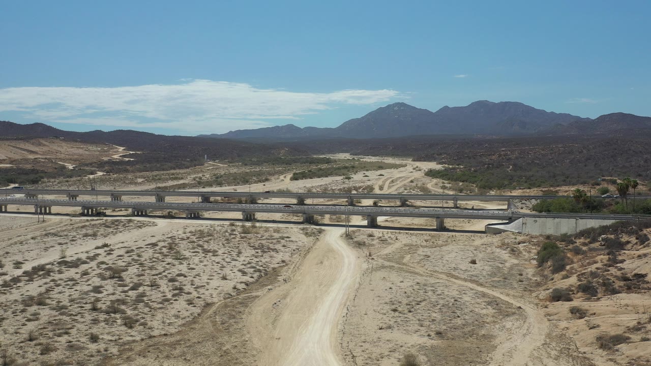 Wide aerial composition of bridge, dirt road, and distant mountains
