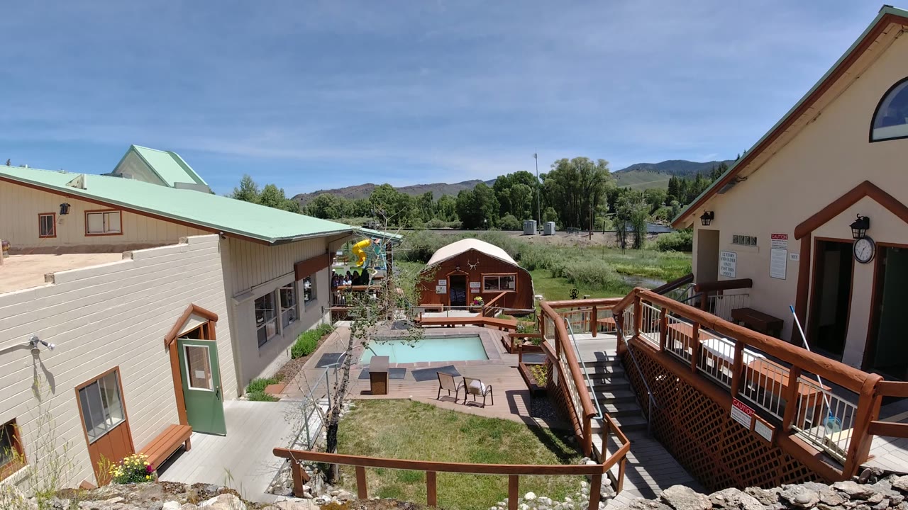Denver, Colorado courtyard view with the pool slightly right of center, a wood ramp in the foreground, beige siding, green rooflines, distant trees, and no visible people.