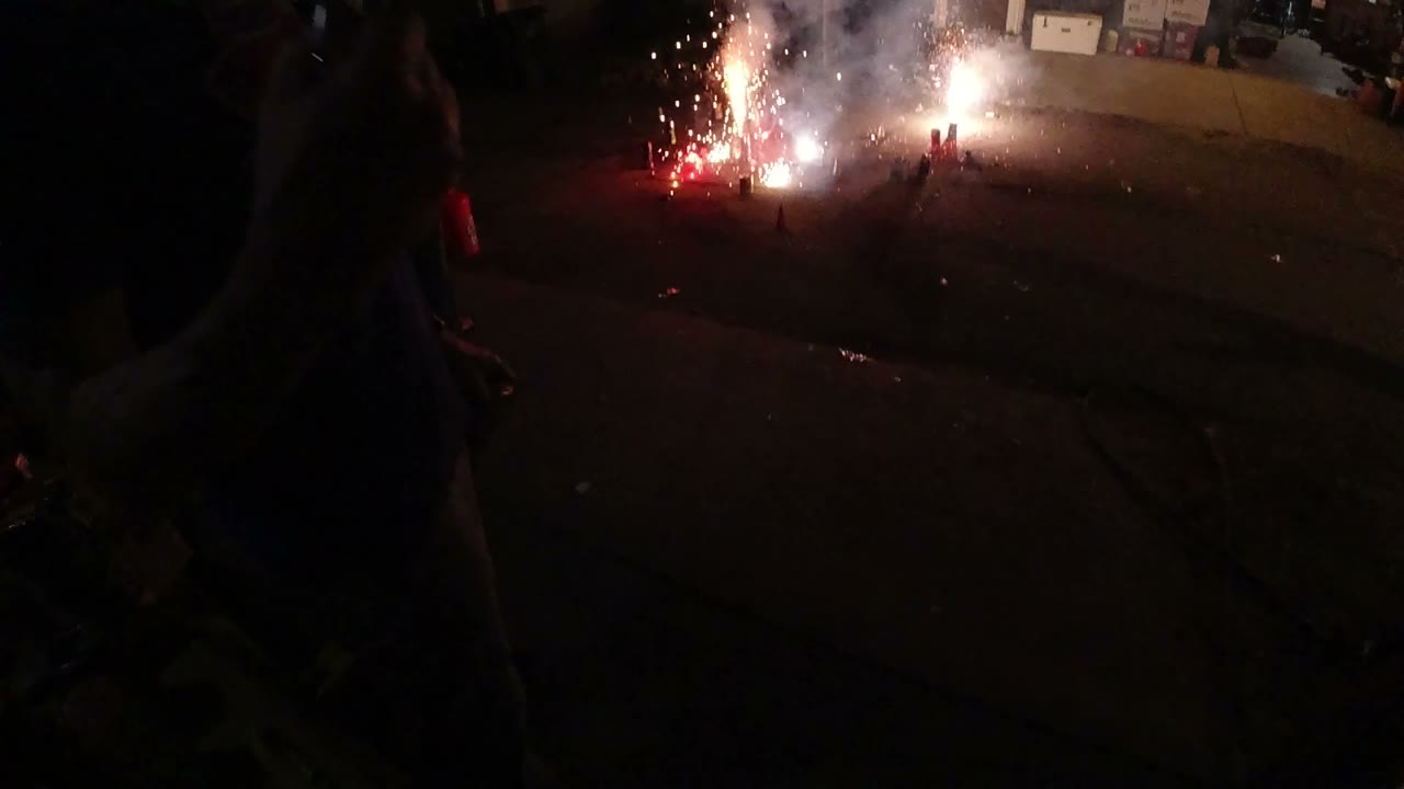 Ground fireworks sparkling on a dark driveway near an open garage.