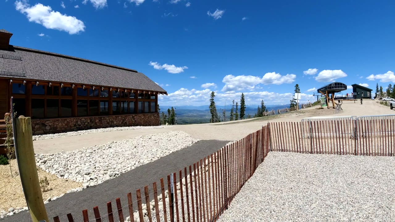 Wood lodge, gravel path, fence, and distant mountains under blue sky.