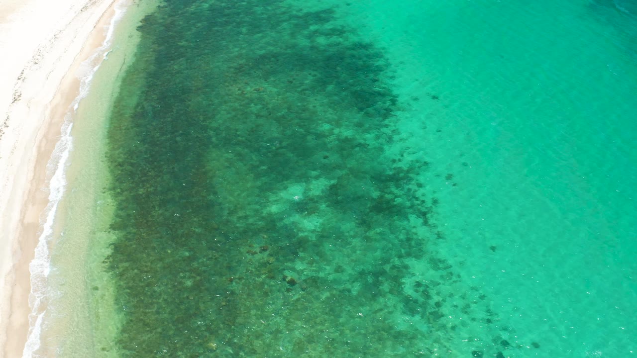 Aerial view of the El Sargento La Ventana beach edge with a narrow surf line, broad submerged dark areas, and no visible people.