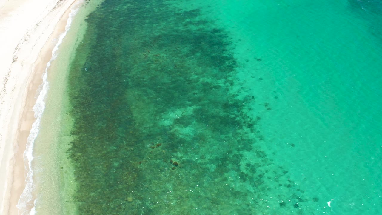 High overhead frame in El Sargento La Ventana showing bright sand, a soft white wave trace, clear turquoise water, and no visible people.