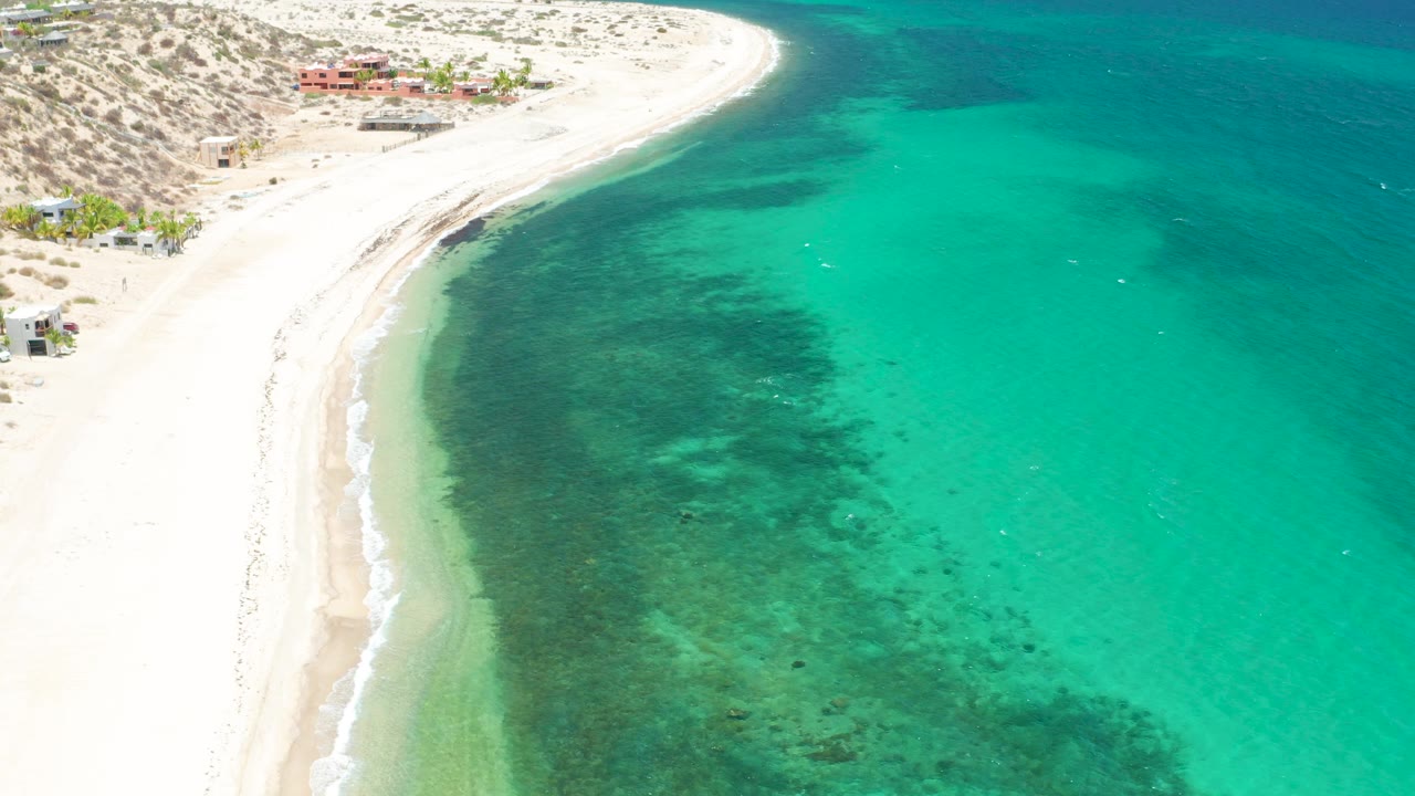 Aerial coastline with sand, surf, and shallow blue water.