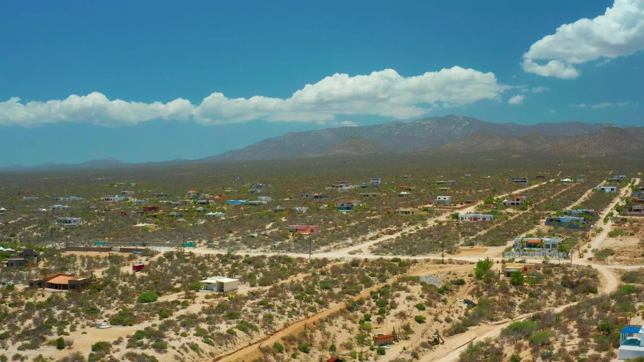 Wide desert town with sandy roads and mountains under clouds.
