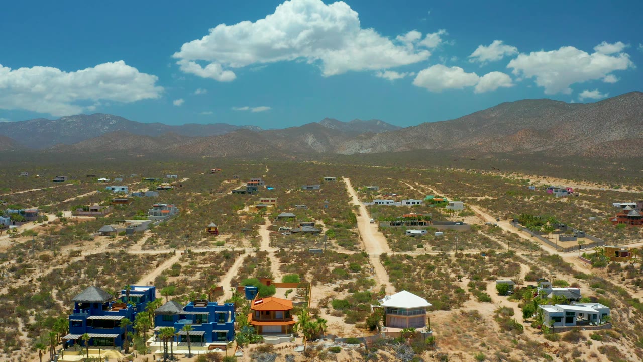 Third frame shows the elevated view across the dry El Sargento La Ventana neighborhood, with colorful rooftops near the lower edge, open lots, mountains, bright clouds, and no visible people.