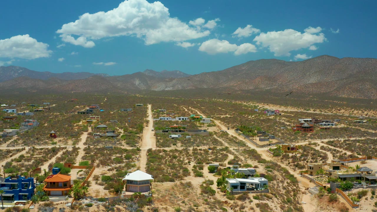 Aerial view of desert roads, homes, and mountains under bright clouds