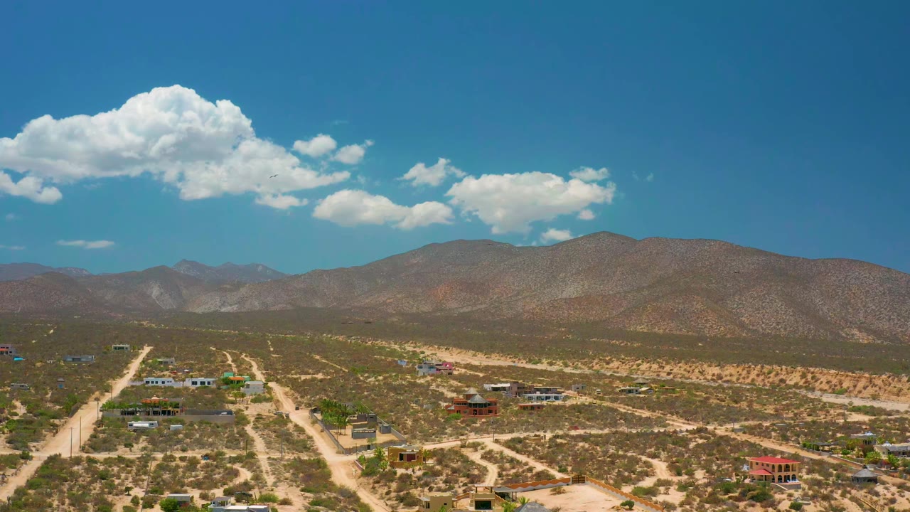 High view across dirt roads, sparse buildings, desert brush, and mountain horizon