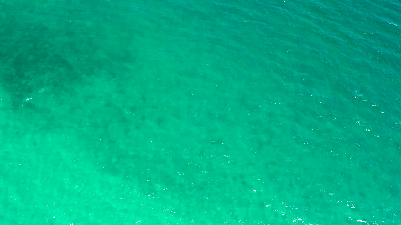 Overhead teal water in El Sargento La Ventana, Mexico, with darker patches beneath the surface, small white flecks, and no visible people.