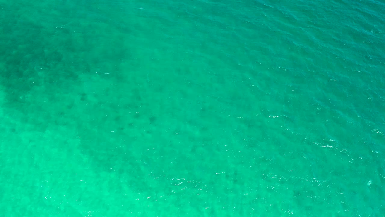 Overhead teal ocean water in El Sargento La Ventana, Mexico, showing scattered white highlights, mottled darker patches below the surface, and no visible people.