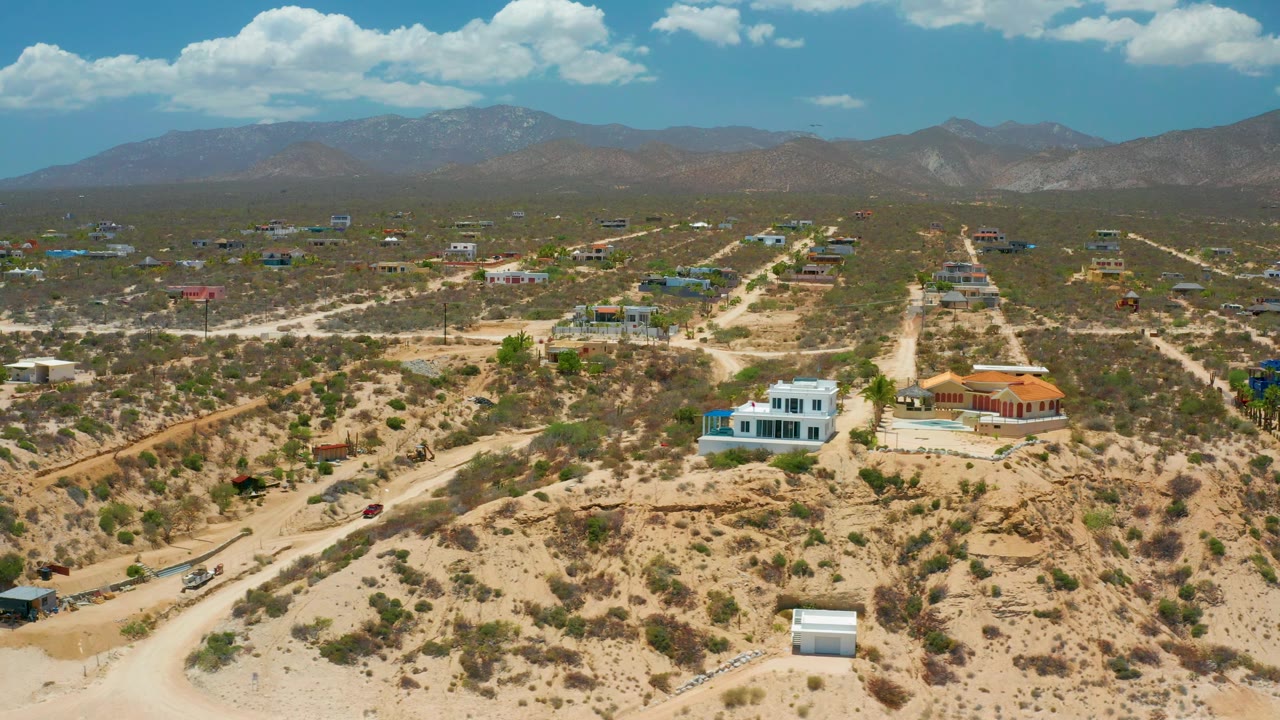 Aerial frame in El Sargento La Ventana, Mexico, with dirt roads running through scrubby desert homes toward a hazy mountain ridge and no visible people.