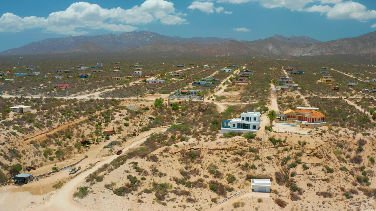 Wide aerial of sparse desert housing with mountains in the background.