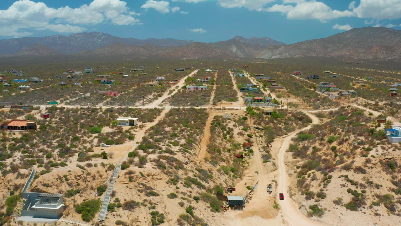 A wide El Sargento La Ventana, Mexico frame shows unpaved roads leading through scrub-covered lots, scattered structures, hazy brown mountains, and no visible people.