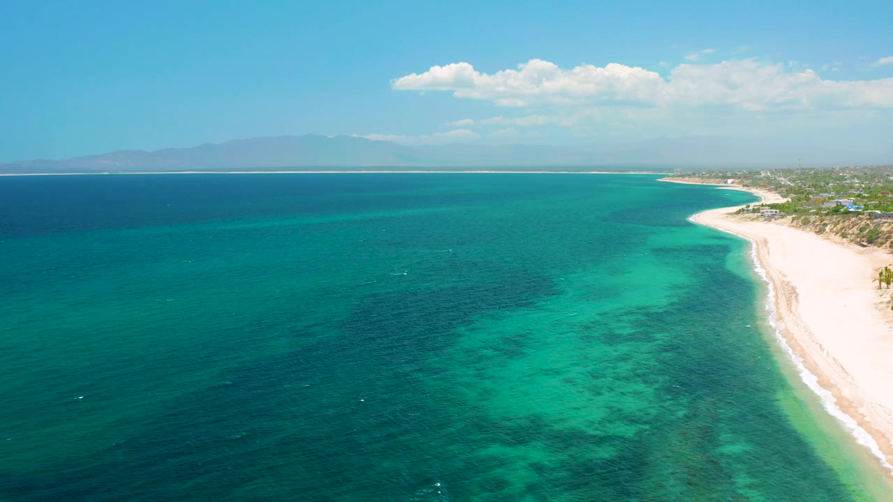 Wide aerial frame from El Sargento La Ventana, Mexico, with open blue sea on the left, turquoise shallows in the middle, beach along the right edge, and no visible people.