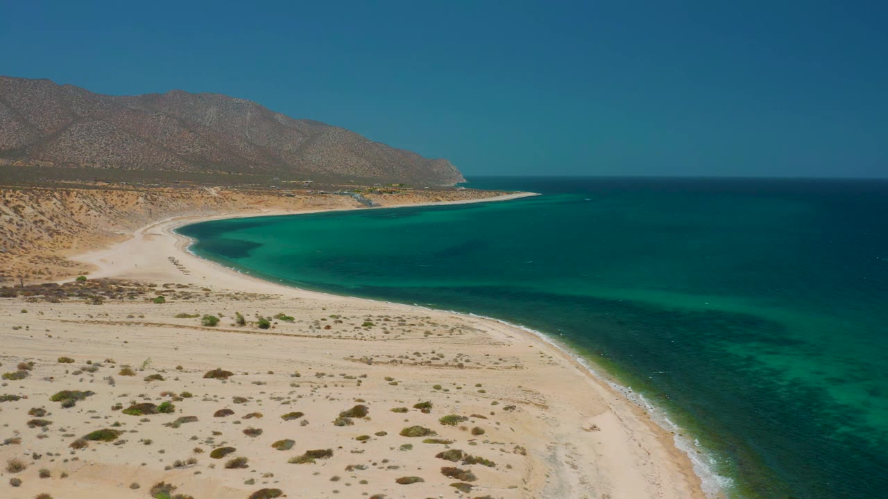 Curving shoreline beside blue-green water and desert mountains.