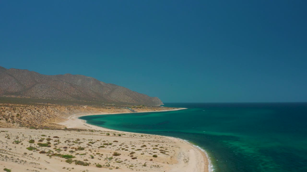 Desert shoreline and green-blue bay under clear sky
