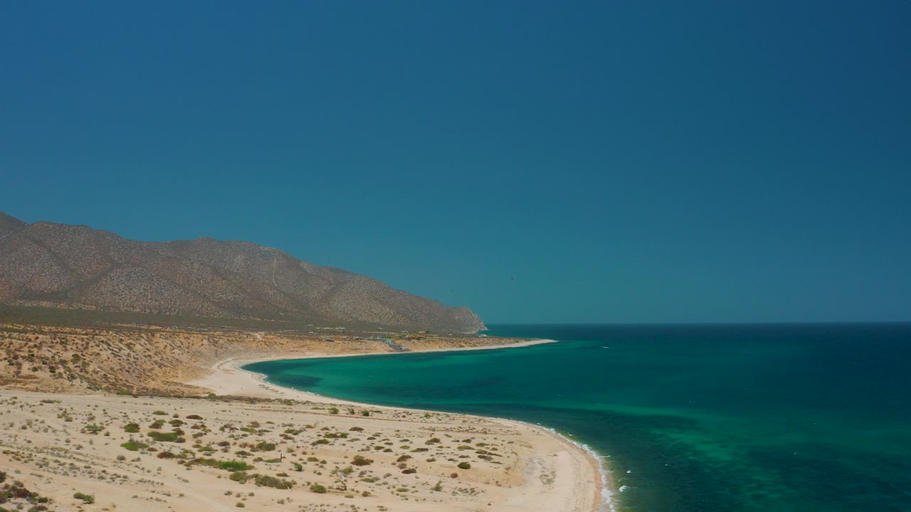 Aerial view of a curved sandy beach beside blue ocean and mountains