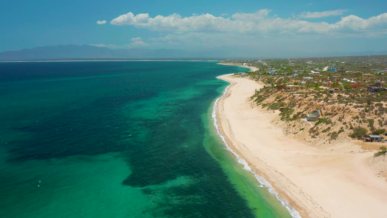 At 0:02, more deep blue water fills the left side while the pale beach curves into the distance at El Sargento La Ventana, Mexico, with no visible people.
