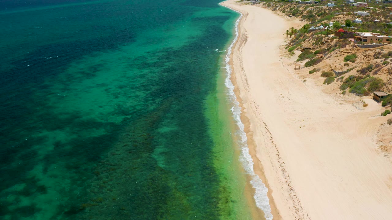 High drone view of the El Sargento La Ventana shoreline with green-blue water filling most of the frame, a narrow surf edge, sand, and no visible people.