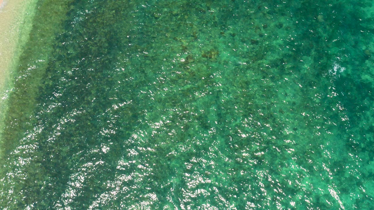 Opening overhead view of turquoise and green water at El Sargento La Ventana, Mexico, with a pale nearshore strip on the left and no visible people.