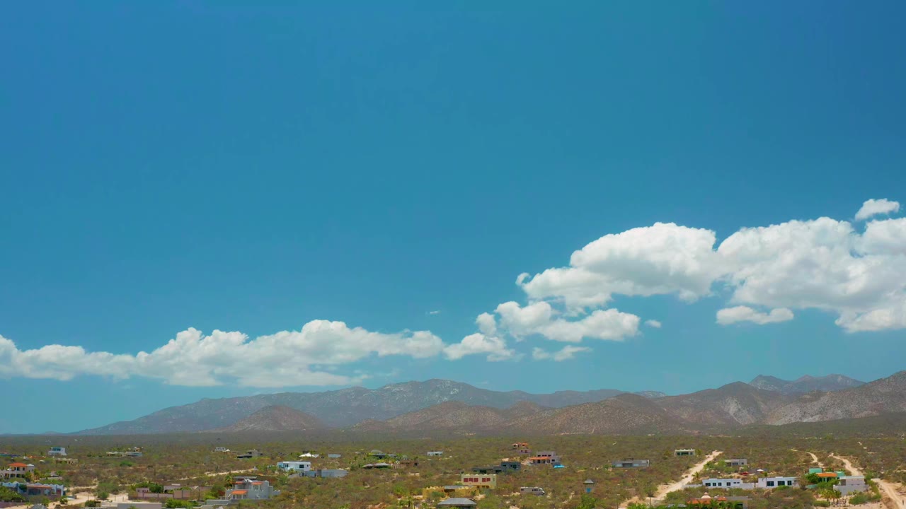 Clouds over mountain ridges and scattered buildings in dry terrain.