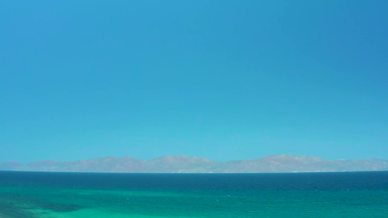 Opening frame of the El Sargento La Ventana, Mexico clip with a broad blue sky, dark ocean band, turquoise shallows, distant mountains, and no visible people.