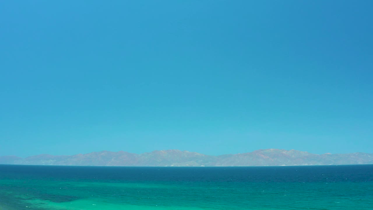 At two seconds, the frame shows layered blue and green water beneath a cloudless sky, with a faint mountain range across the horizon and no visible people.