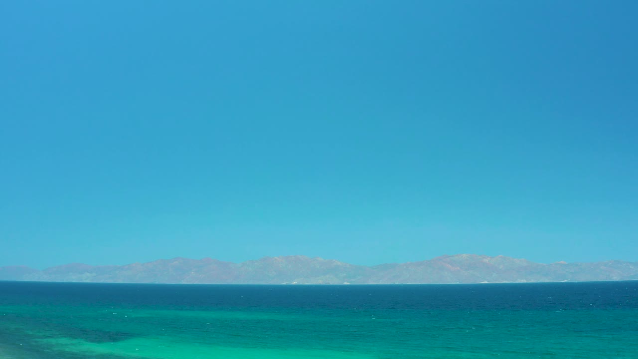 Distant mountains and open water under bright midday sky